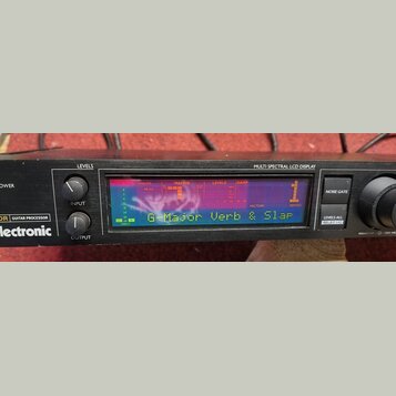 Černý kytarový procesor s nápisem electronic a označením GUITAR PROCESSOR. Zařízení má Multi Spectral LCD Display, na kterém je zobrazen text G-Major…