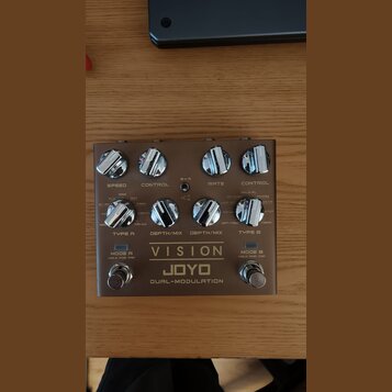 Kytarový efekt pedál v šedé barvě s kovovým povrchem. Na spodní části je nápis VISION, JOYO a DUAL-MODULATION. Zařízení má osm ovládacích knoflíků, d…