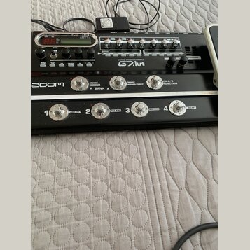 Černý kytarový procesor s nápisem GUITAR EFFECTS CONSOLE G2.1ut a logem ZOOM. Zařízení má digitální displej, několik ovládacích knoflíků a čtyři stou…