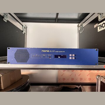 Modré rackové zařízení s nápisem MIDAS DL151 audio system I/O. Na předním panelu jsou umístěny kontrolky, displej a tlačítka s nápisy menu, select a…