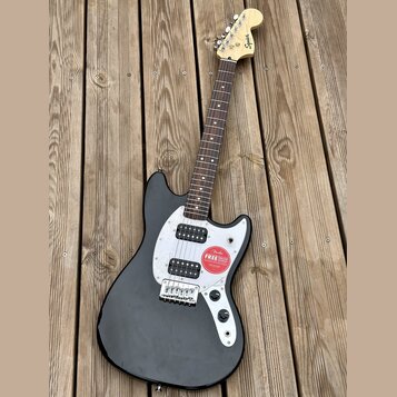 Černá elektrická kytara s bílým pickguardem a hnědým hmatníkem. Na hlavě je viditelné logo Squier. Kytara má dva snímače a na těle je nalepená červen…