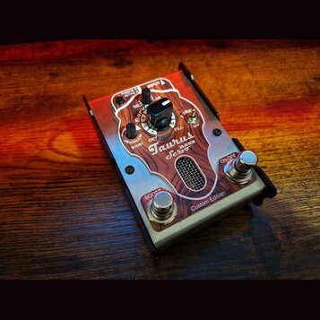 Kytarový efekt s kovovým šasi a dřevěným panelem v přední části. Na panelu jsou nápisy Taurus BASS Servo, Custom Edition a označení ovládacích prvků…