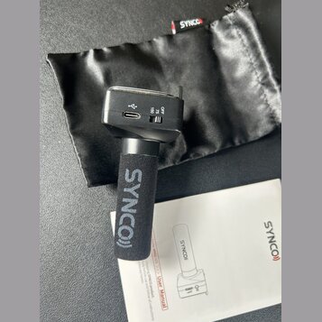 Černý mikrofon s větrolnicí, na které je bílý nápis SYNCO)). Na těle mikrofonu jsou vidět přepínač s označením OFF, 75 a 150 a USB-C port. Součástí j…