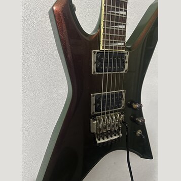 Elektrická kytara s tmavě hnědým kovovými lakem a hranatým tvarem těla. Nástroj má dva humbuckery, tremolo systém a dvě ovládací knoflíky. Na těle ne…