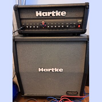 Kytarové kombo typu stack značky Hartke. Horní část tvoří zesilovač s ovládacími prvky, kde jsou viditelné nápisy INPUT, CRUNCH, VOLUME, BASS, TREBLE…