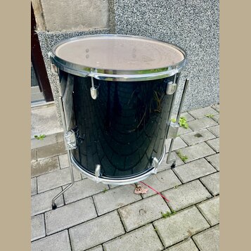 Černý buben s chromovanými obručmi a ladicími šrouby, umístěný na kovovém stojanu. Povrch bubnu je lesklý a vykazuje drobné odpady a znečištění. Na n…