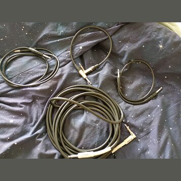 Čtyři černé instrumentní kabely různých délek položené na tmavé látce s motivem hvězd. Na jednom z konektorů nejdelšího kabelu je viditelný nápis Fen…