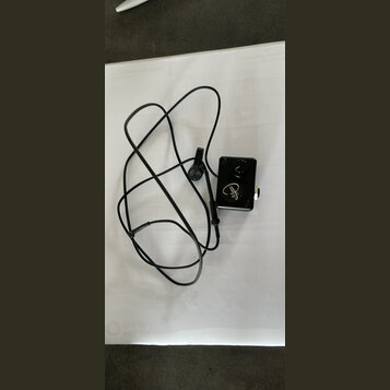 Černý kabel s malým čtvercovým ovládacím modulem. Na modulu je bílý nápis v kurzívě "Alba". Kabel končí malým kulatým senzorem s připevňovacím klipem.