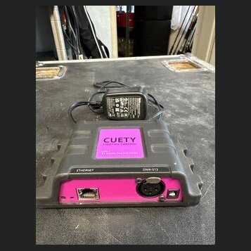Šedý plastový přístroj s růžovými prvky a nápisem CUETY. Na zadní straně jsou viditelné konektory označené jako ETHERNET a DMX-512. K přístroji je př…