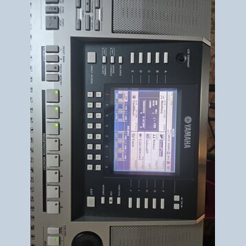 Detailní záběr na ovládací panel digitálního klavíru značky YAMAHA. Uprostřed je LCD displej zobrazující nastavení s nápisy jako NewSong, Cool8Beat a…