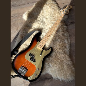 Elektrická basová kytara s tělem v provedení sunburst a zlatým pickguardem. Na hlavě hředu je viditelné logo Squier. Nástroj má světlou dřevěnou hmat…