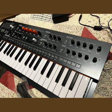 Klávesový synthesizátor s černým šasi a ovládacími prvky v horní části. Na pravé straně je nápis MINITEK. Panel obsahuje různé potenciometry, přepína…