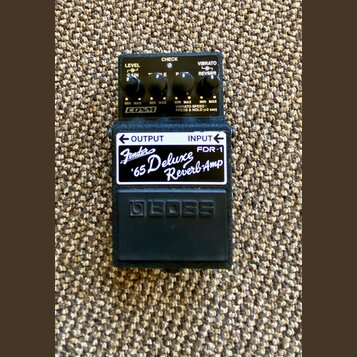 Černý kytarový pedál s nápisem Fender '65 Deluxe Reverb-Amp a označením modelu FDR-1. Na horní části jsou čtyři ovládací knoflíky s popisky LEVEL, GA…