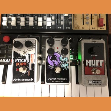 Tři kytarové efekty značky electro-harmonix umístěné vedle sebe na klávesovém nástroji. Zleva je bílý pedál s nápisem PITCH FORK, prostřední je černý…