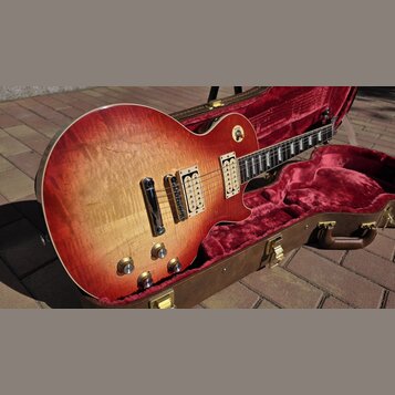 Elektrická kytara s tónem sunburst v červeně a žluté, umístěná v hnědém kufru s červeným plyšovým vnitřkem. Nástroj má dva humbuckery, čtyři otočné k…