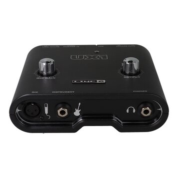 Černý zvukový interface s nápisy UX1 a LINE 6. Na horní straně jsou dva kovové otočné ovladače s popisky MIC GAIN a OUTPUT. V dolní části jsou vstupy…