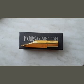 Zlatý kovový mouthpiece na saxofon položený na černé krabičce. Na krabičce je bílý nápis NADIRSAXWIND.COM a na mouthpieceu je vyryté logo TD. Povrch…