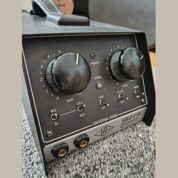 Černý rackový přístroj s nápisem UNIVERSAL AUDIO SOLO/610 Classic Vacuum Tube Mic Pre & DI Box. Přední panel obsahuje dva velké černé otočné ovladače…