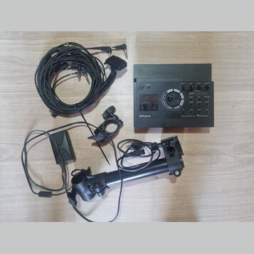 Na fotografii je elektronický bicí modul značky Roland s nápisem V-Drums a Drum Sound Module TD-70C. K modulu patří několik černých kabelů s různými…