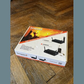 Kartonová krabice s oranžovým potiskem, na které je nápis VHF wireless microphone · radiomicrofono VHF a značka bespeco. Na obalu jsou zobrazeny dva…