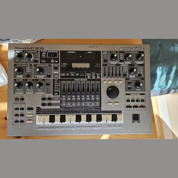 Stříbrný sekvenční sampler Roland MC-505 groovebox. Na předním panelu jsou viditelné nápisy Roland MC-505 a groovebox, řada ovládacích knoflíků, posu…