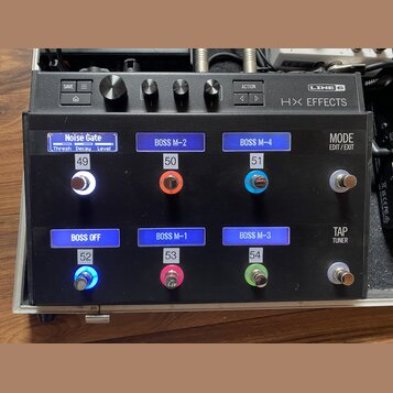 Černý kytarový efektový pedalboard s nápisem LINE 6 HX EFFECTS. Horní část obsahuje ovládací knoflíky a tlačítka SAVE, ACTION a HOME. Spodní část obs…