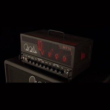 Černý kytarový zesilovač s kovovou mřížkou a rukojetí na horní straně. Na přední straně je bílý nápis Paul Reed Smith a červený nápis MT15. Spodní pa…