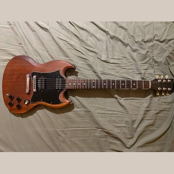 Elektrická kytara s hnědým dřevěným povrchem a černým pickguardem. Na hlavě je viditelné logo Gibson. Kytara má dva humbuckery, čtyři ovládací knoflí…