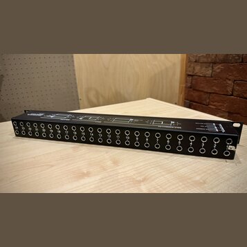 Černý rackový patchbay s řadou 24 zapojovacích jackových konektorů. Nad konektory jsou bílé nápisy s čísly od 1 do 24 a technické schéma zapojení. Na…