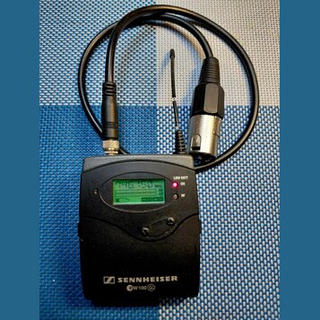 Černý bezdrátový přijímač s nápisem SENNHEISER a označením EW 100 G2. Zařízení má malý LCD displej s indikátory MHz, RF, AF a Pilot, oraz tlačítko MU…