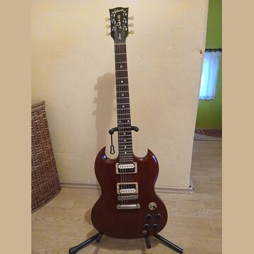Tmavě hnědá elektrická kytara s dvojstupňovými humbuckery, umístěná na černém stojanu. Na hlavě nástroje je bílý nápis Gibson a pod ním v kurzivě Epi…