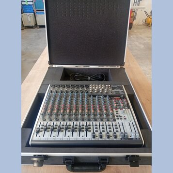 Míchací pult v ochranném přepravním kufru s černým polstrováním. Na horním pravém rohu je viditelné logo "Behringer". Zařízení obsahuje řadu faderů,…