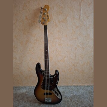 Elektrická basová kytara s tělem v provedení sunburst a hnědým hmatníkem. Na hlavě je viditelné logo Fender a nápis Jazz Bass. Kytara má tmavý pickgu…