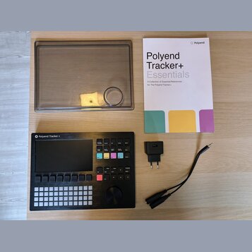 Na fotografii je černý sekvencer Polyend Tracker + s displejem a řadou tlačítek. Součástí sady je průhledný plastový kryt, napájecí adaptér a printed…