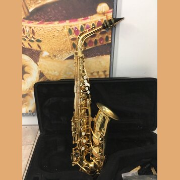 Zlatý saxofon umístěný v otevřeném černém kufru. Na zvonu nástroje je viditelné logo a nápis "YAMAHA". Povrch instrumentu je lesklý, s bílými odpoutá…