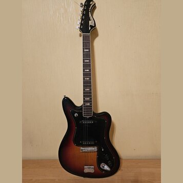 Elektrická kytara s trupem v tmavém sunburst provedení a černým pickguardem. Na hlavě hředu je bílý nápis „Musima der Luther“. Nástroj vykazuje známk…