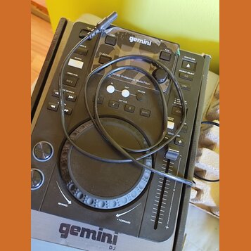 Černý digitální DJ player s nápisem gemini a označením CDJ-300 Professional Media Player. Zařízení obsahuje jogové kolo, fader a řadu ovládacích tlač…