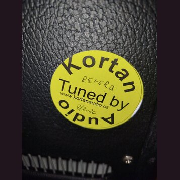 Kruhová žlutá nálepka s černým textem nalepená na černém povrchu z imitace kůže. Na nálepce je nápis Kortan Tuned by Audio a webová adresa www.kortan…