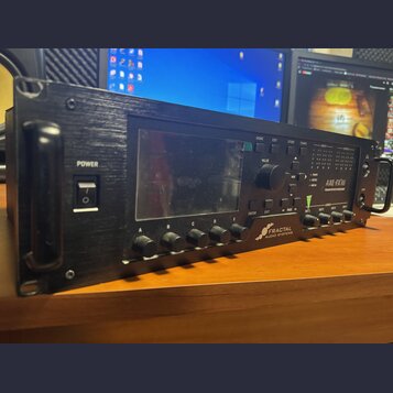 Černý rackový kytarový procesor s displejem a ovládacími prvky. Na předním panelu jsou nápisy POWER, FRACTAL AUDIO SYSTEMS a AXE-FX III. Zařízení má…