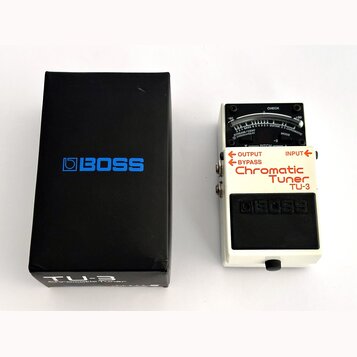 Bílá kytarový ladič s černým pedálem a displejem. Na přístroji jsou nápisy „OUTPUT“, „BYPASS“, „INPUT“, „Chromatic Tuner TU-3“ a logo „BOSS“. Vedle l…
