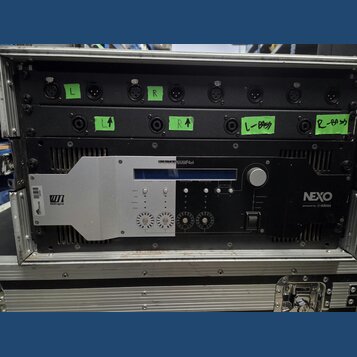 Černý rackový zesilovač značky NEXO s nápisem powered by YAMAHA a označením DIGITAL NXAMP4x4. Zařízení je umístěno v transportním kufru a má stříbrný…