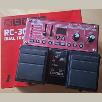 Červený pedalboard s nápisy RC-30 DUAL TRACK LOOPER a Loop Station. Zařízení má ovládací prvky pro LOOP FX, MEMORY, RHYTHM a MIC, včetně dvou černých…