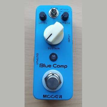 Modrý kytarový efekt s nápisem Blue Comp a značkou MOOGER. Na horní straně jsou dva černé otočné knoflíky s popisky LEVEL a ATTACK, přepínač Treble/N…