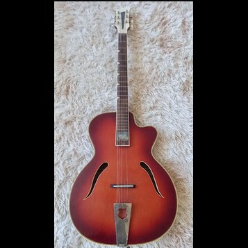 Kytara s polodubnovým tělem v červenohnědém sunburst provedení. Na hmatníku je viditelný světlý nápis, který není čitelně rozlučitelný. Nástroj vykaz…