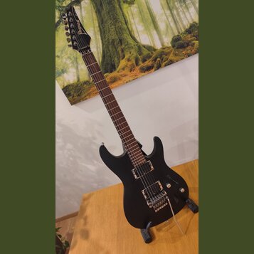 Černá elektrická kytara s matným povrchem a tmavým hmatníkem. Na hlavě je viditelné logo Ibanez. Nástroj má dva humbuckery, ovládací knoflíky a strun…