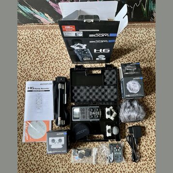 Sada obsahuje digitální nahrávač Zoom H6 v černém přepravním kufru s pěnovou výplní. K zařízení patří manuál s nápisem H6 Handy Recorder, CD s nápise…