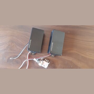 Dvě černé elektrické kytarové snímače s nápisem Seymour Duncan. Jsou vybaveny připojovacími kabely a k nim je přiložen jeden potenciometr s připojený…