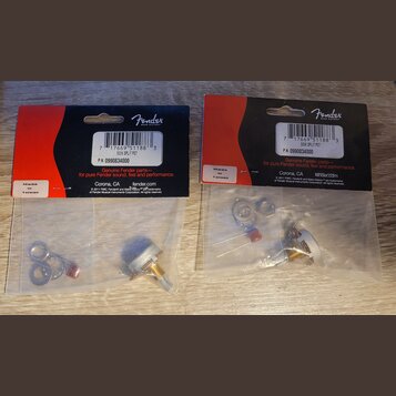 Dvě balená příslušenství značky Fender v plastových sáčcích s červeným a černým kartonem. Na obou je uveden nápis Genuine Fender parts, P.N. 09908340…