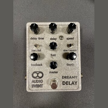 Stříbrný efektový pedál s nápisy AUDIO EVENT a DREAMY DELAY. Zařízení má šest černých otočných knoflíků s popisky delay time, delay, speed, feedback,…