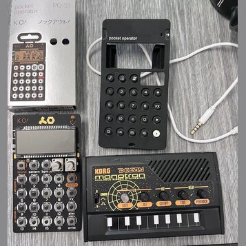 Fotografie zobrazuje tři zařízení značky Korg a doprovodné příslušenství. V horní části je stříbrný kartonový obal s nápisy pocket operator PO-33 K O…